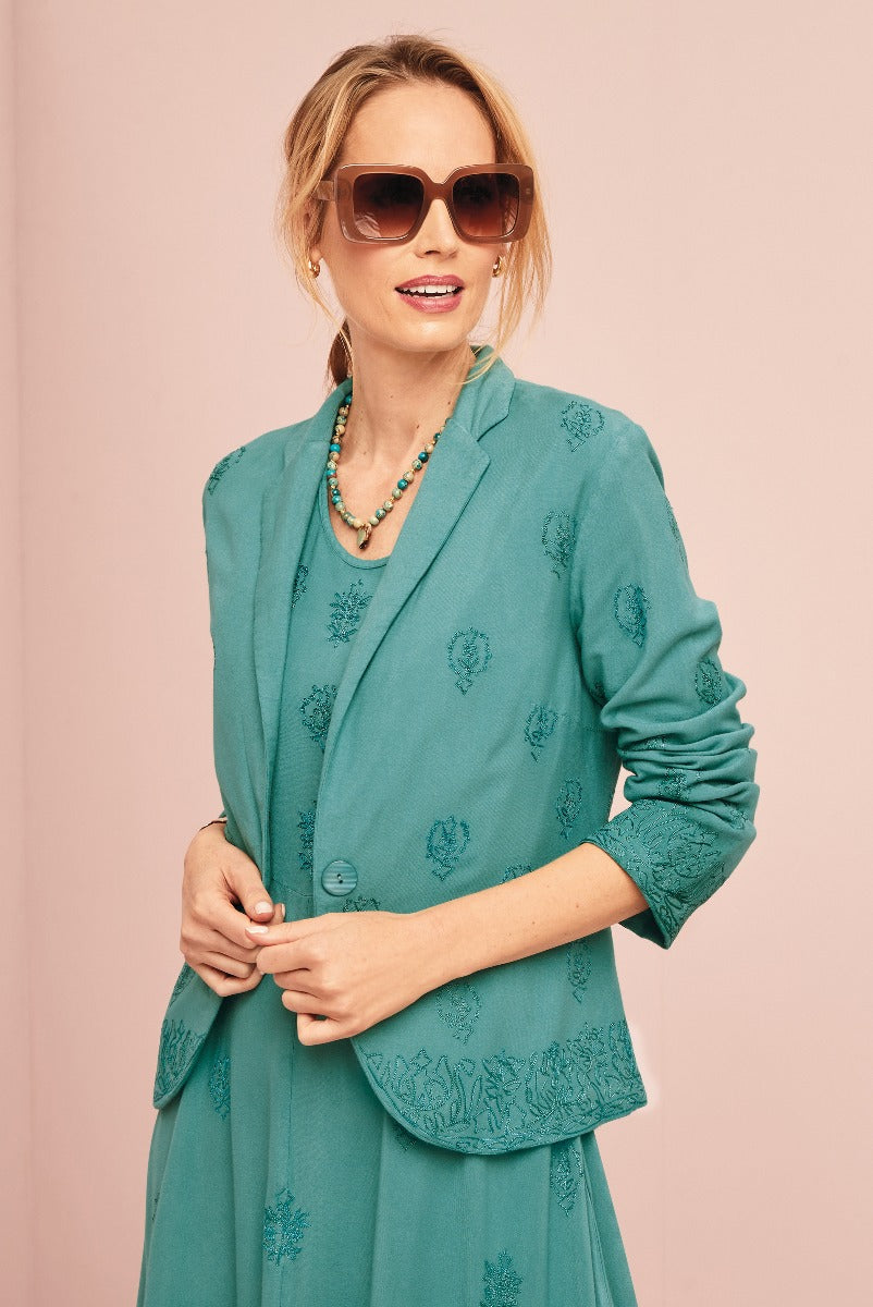 Lily Ella Collection aqua blue embroidered jacket and skirt set, stylish women's workwear, elegant floral pattern, fashion model wearing oversized sunglasses and statement necklace.