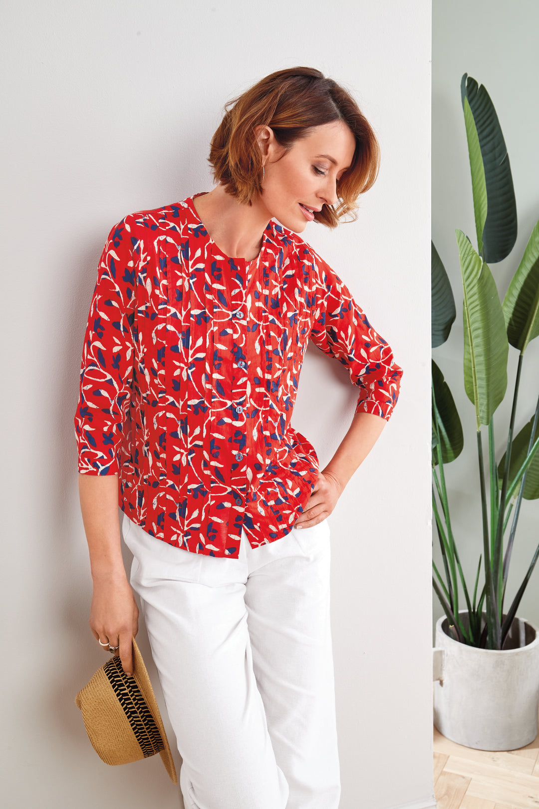 Lily Ella Collection red floral blouse with 3/4 sleeves, stylish women's fashion, paired with white trousers and straw clutch, modern casual elegant look