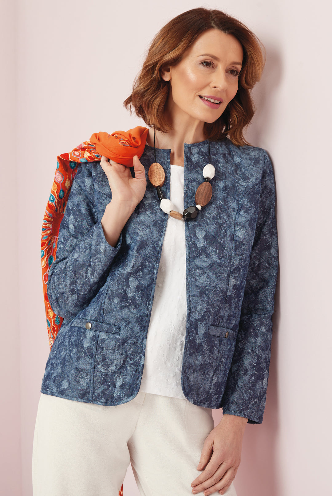 Lily Ella Collection stylish blue textured jacket on model paired with white blouse, cream trousers, and statement necklace, accented by orange patterned scarf.