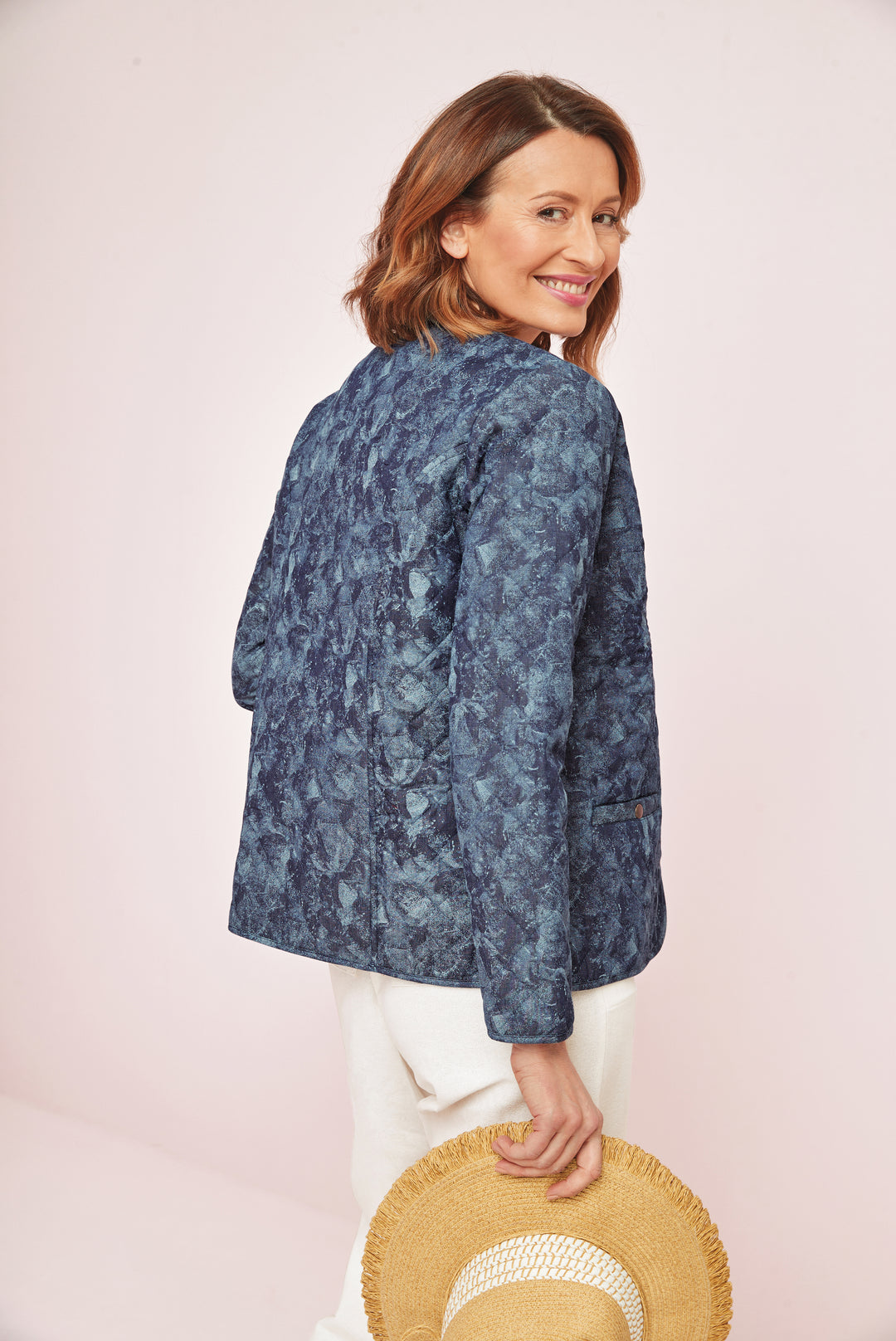 Lily Ella Collection stylish blue patterned jacket for women, rear view of elegant chic outerwear, paired with white trousers and holding straw hat.