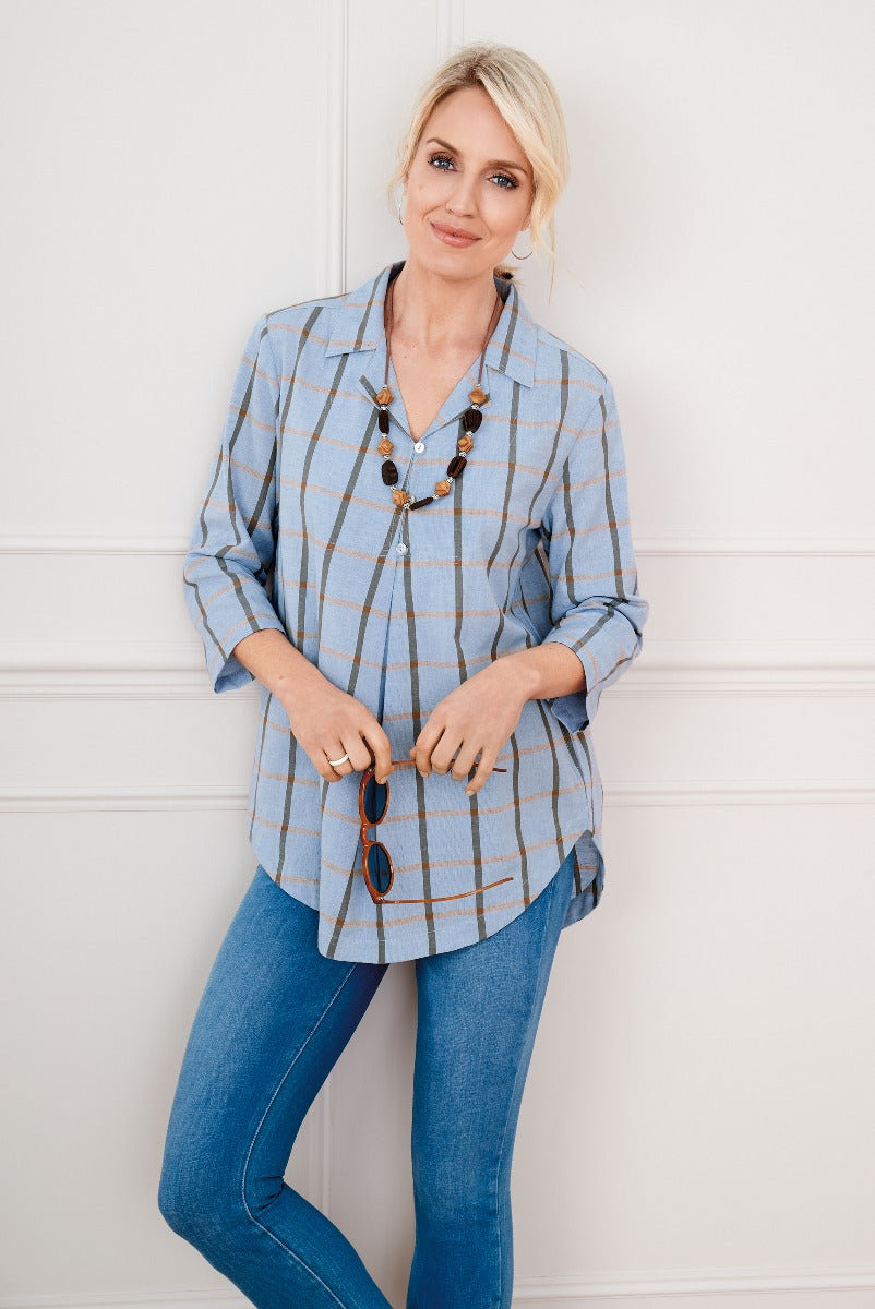 Lily Ella Collection stylish blue and beige checked tunic top on model paired with slim-fit jeans and accessorized with a long beaded necklace, promoting casual chic women's fashion.