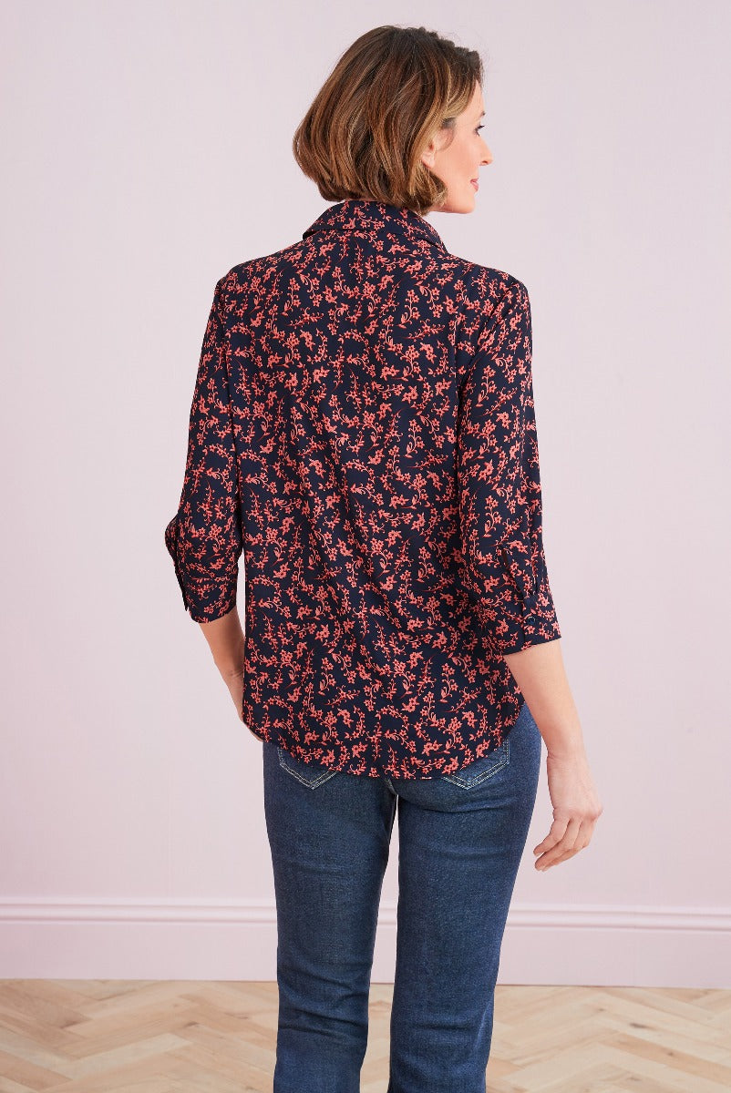 Lily Ella Collection stylish navy and coral floral patterned blouse for women with roll-up sleeves paired with denim jeans, showing back view of outfit.