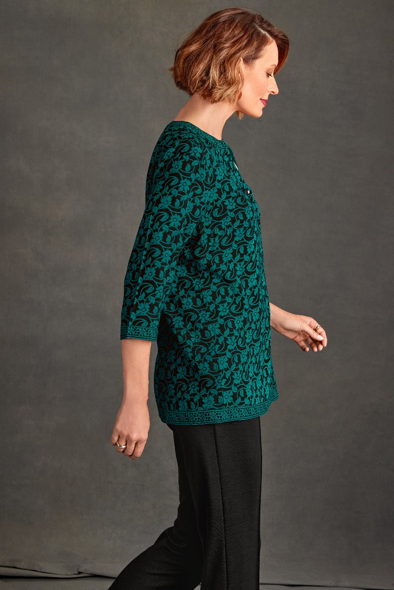 Lily Ella Collection teal patterned tunic top on model with elegant black trousers, stylish women's casual wear, side profile view