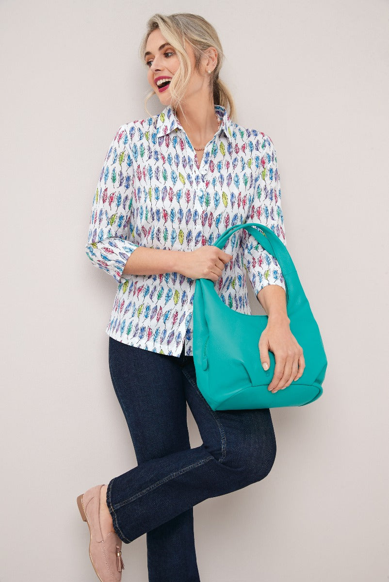 Lily Ella Collection women's fashion featuring a smiling model in a white patterned blouse with feathers design, dark blue denim jeans, and carrying a teal shoulder bag.