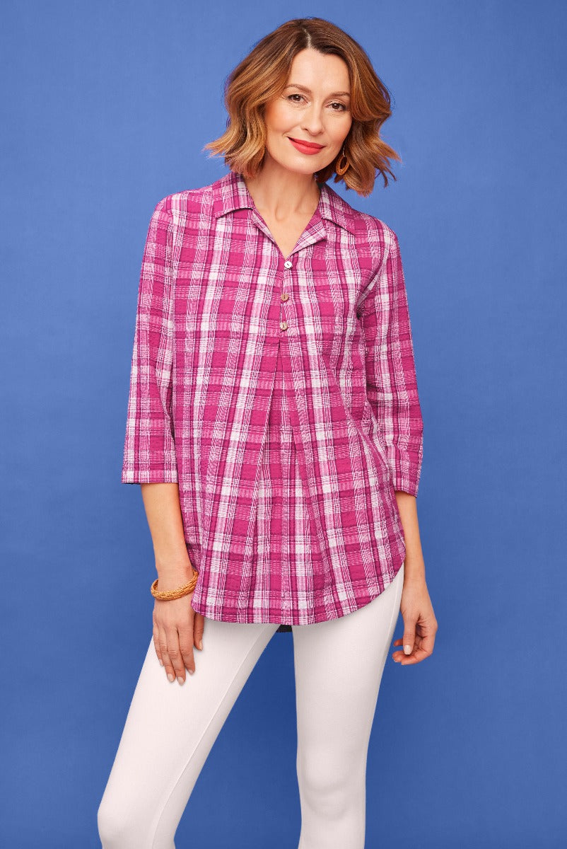 Lily Ella Collection casual pink plaid blouse with three-quarter sleeves paired with white slim-fit trousers on a model against a blue background