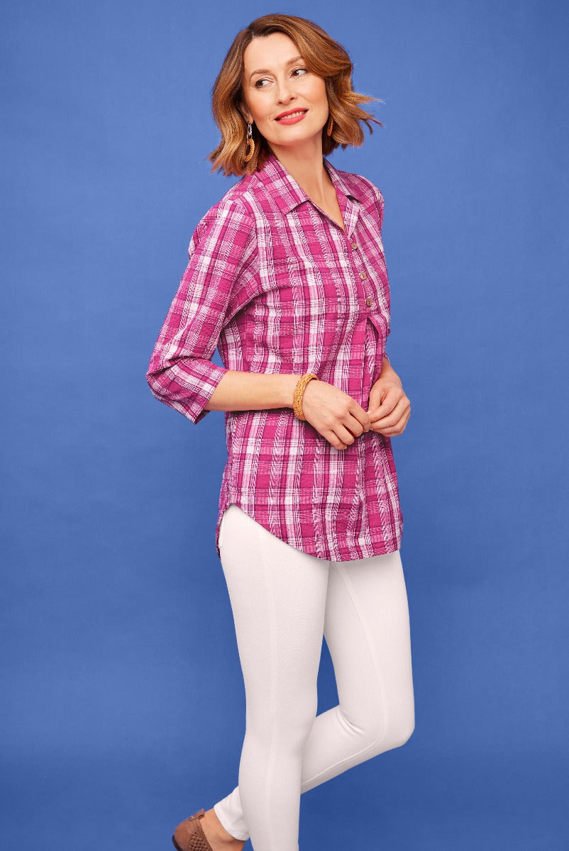 Lily Ella Collection stylish woman wearing pink checkered blouse and white slim-fit trousers with brown loafers on blue background.