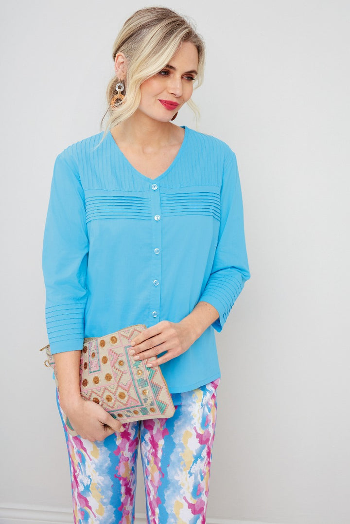 Lily Ella Collection sky blue pleat-detail blouse paired with colorful floral printed trousers and a patterned clutch, elegant casual women's fashion.