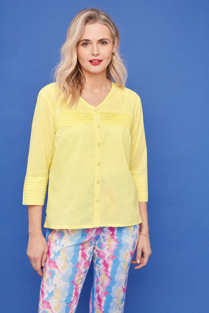 Lily Ella Collection yellow pintuck blouse styled with colorful floral pattern trousers for women, elegant casual spring outfit against blue background.