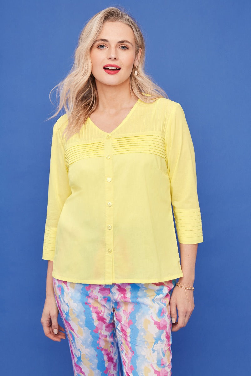 Lily Ella Collection yellow 3/4 sleeve pin-tuck blouse paired with colorful floral trousers against a blue background, showcasing contemporary women's fashion and style.