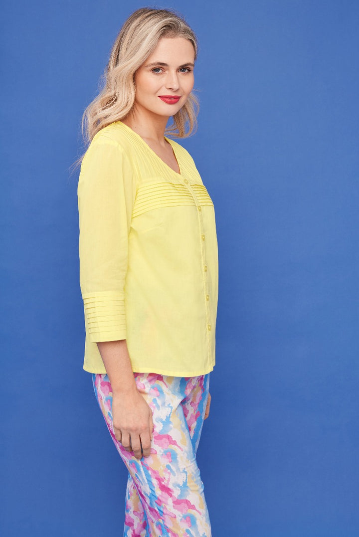 Lily Ella Collection light yellow pin-tuck blouse and colorful abstract print trousers, woman modeling spring fashion with elegant casual wear against blue background