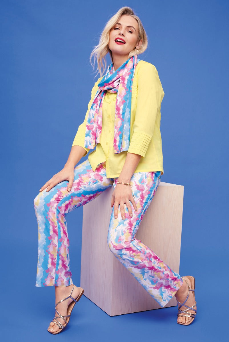 Lily Ella Collection vibrant yellow cardigan paired with colourful floral print trousers and a blue patterned scarf, model posing with confidence against a blue background, stylish women's spring fashion outfit.