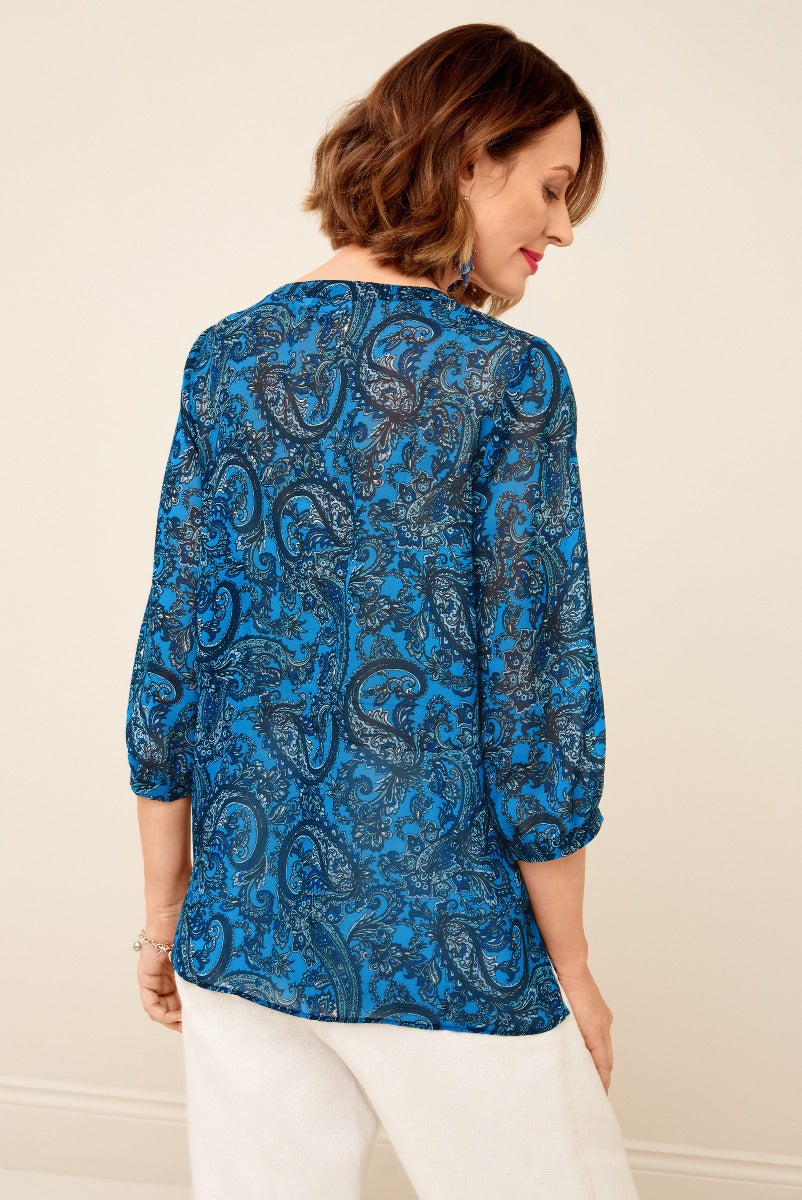 Lily Ella Collection blue paisley print blouse, stylish women's long sleeve top, elegant casual wear, rear view on model with white trousers.