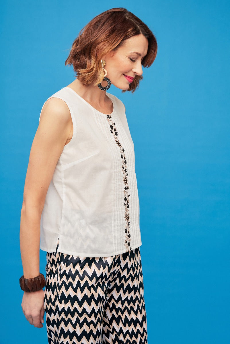 Lily Ella Collection elegant ivory sleeveless blouse with detailed embroidery, paired with chevron patterned trousers, fashion-forward women's wear on a blue background