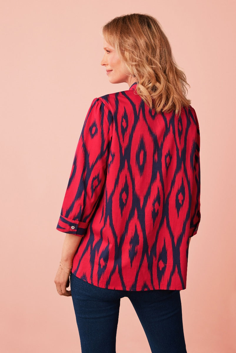 Lily Ella Collection red and navy Ikat print blouse, stylish women's top with three-quarter sleeves, elegant casual wear, model posing against pink background