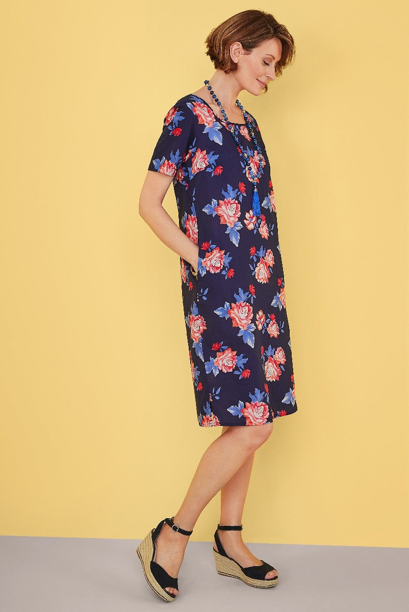 Lily Ella Collection navy floral dress, stylish women's knee-length summer dress with red and blue roses, casual elegant fashion, model showcasing outfit with coordinating accessories and espadrille wedge sandals.
