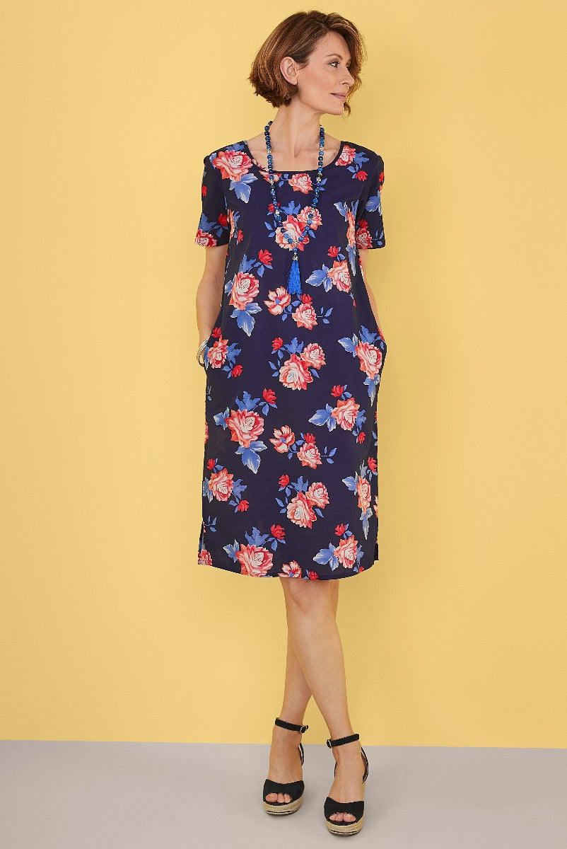 Lily Ella Collection navy blue floral dress, elegant short sleeve summer style, women's fashion, paired with black ankle strap heels against a vibrant yellow background.