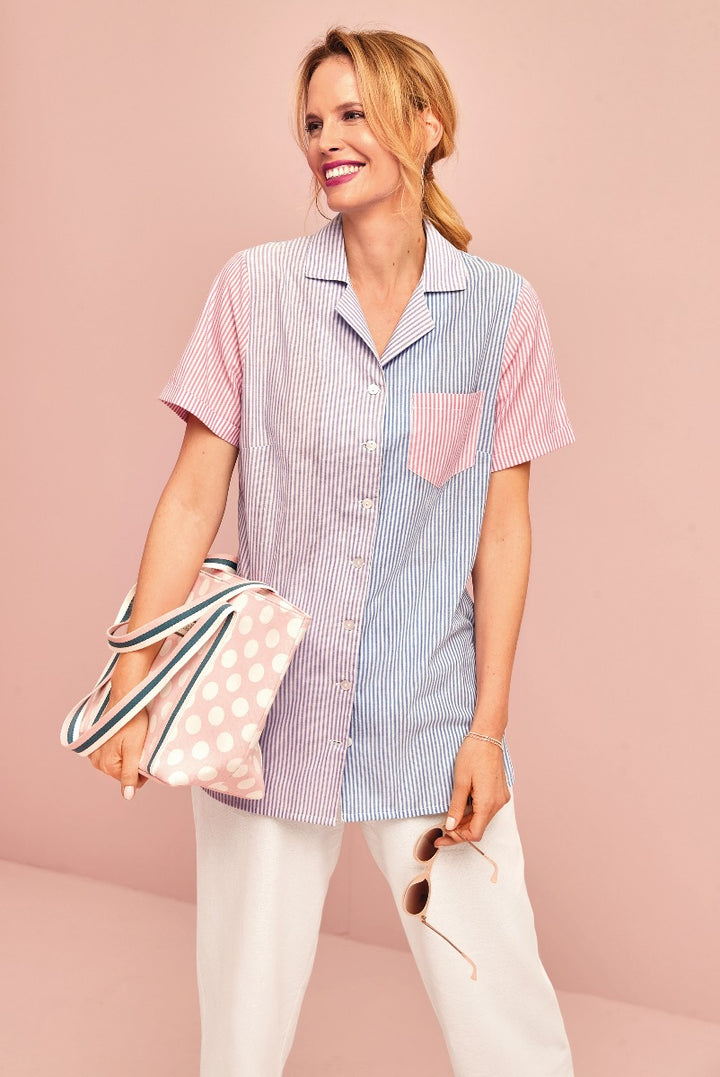 Lily Ella Collection stylish two-tone striped button-up shirt in pink and blue, model pairing it with white trousers and a polka-dot accessory bag on a soft pink background.