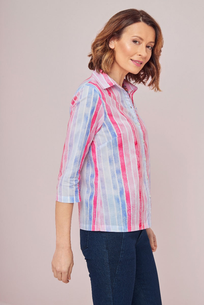 Lily Ella Collection model showcasing a casual striped blouse in pastel pink and blue with classic collar and rolled-up sleeves, paired with dark denim jeans for a stylish everyday look.