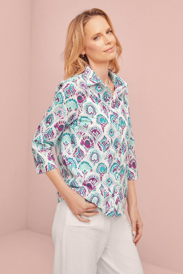 Lily Ella Collection women's fashion model showcasing a paisley pattern teal and purple blouse with a classic collar and white trousers, reflecting modern style and comfort