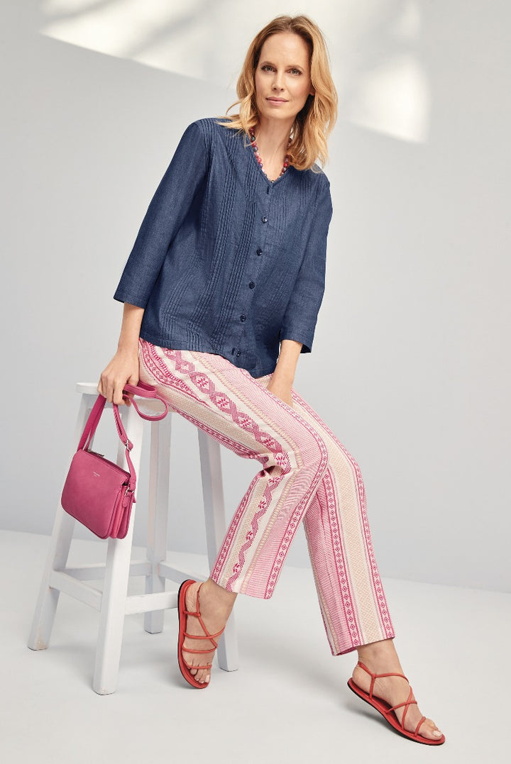 Woman posing in Lily Ella Collection attire, featuring a navy button-down blouse, pink patterned trousers, and coordinating sandals with a matching pink shoulder bag, highlighting casual chic style and comfort.