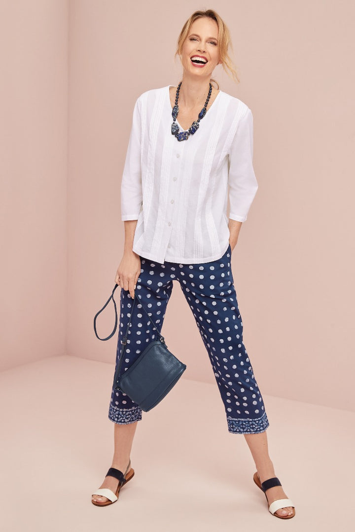 Lily Ella Collection white linen-blend tunic top with navy blue printed capri trousers, accessorized with statement necklace and leather crossbody bag on smiling model against pastel background.
