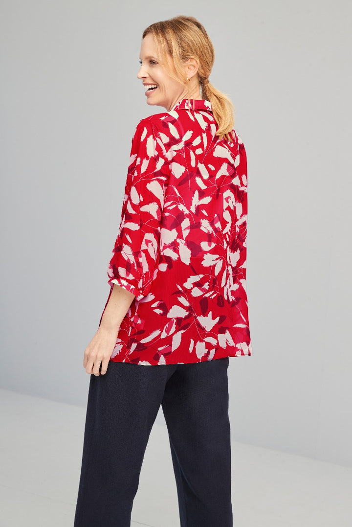 Woman modeling a Lily Ella Collection red floral print blouse with three-quarter sleeves and navy trousers, stylish casual wear.