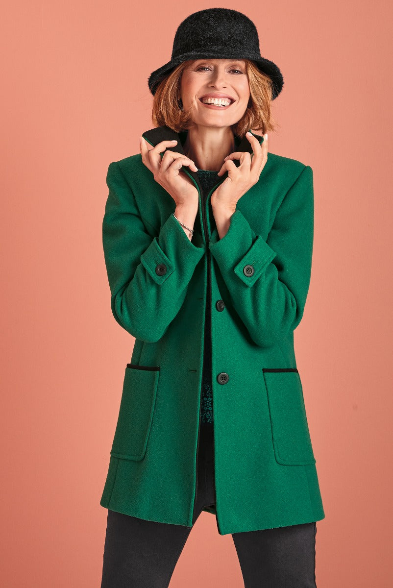 Lily Ella Collection stylish emerald green coat on model with elegant black hat, showcasing contemporary women's outerwear fashion.