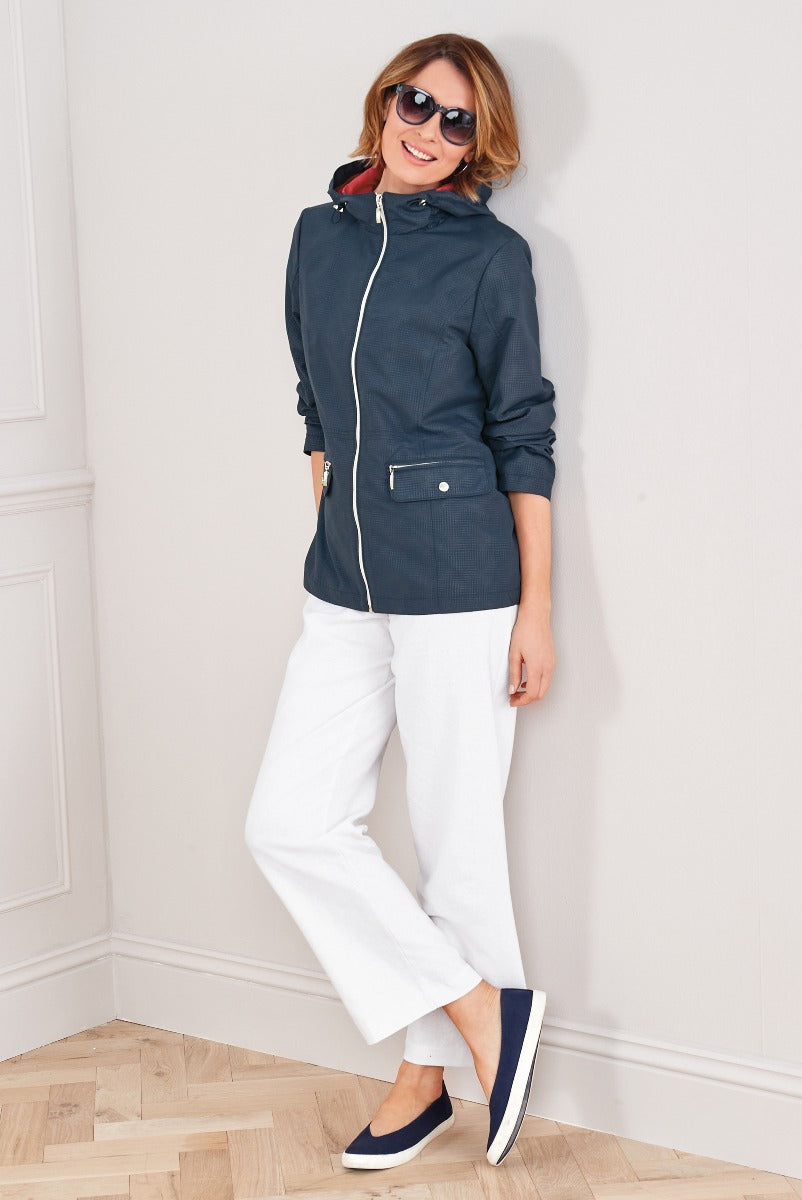Lily Ella Collection navy casual jacket with white trim and white linen trousers on smiling model with sunglasses and navy slip-on shoes.
