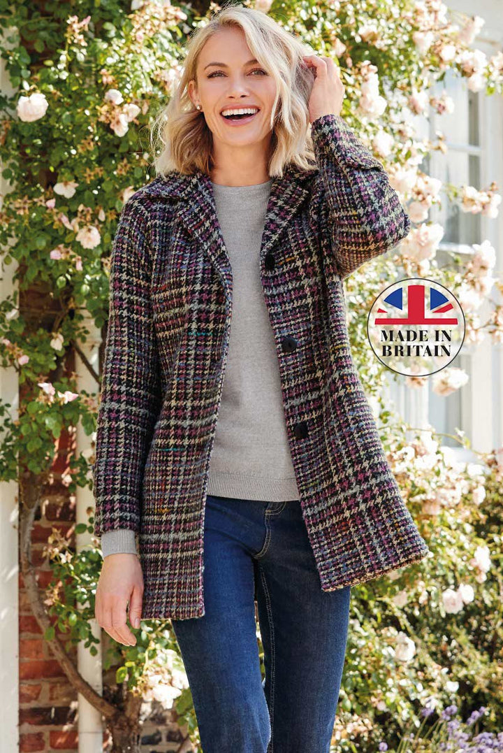 Lily Ella Collection women's multicolored tweed jacket, Made in Britain, featuring a stylish woman in a vibrant plaid patterned coat, casual grey sweater, and blue jeans, posing with a warm smile in a charming garden setting.