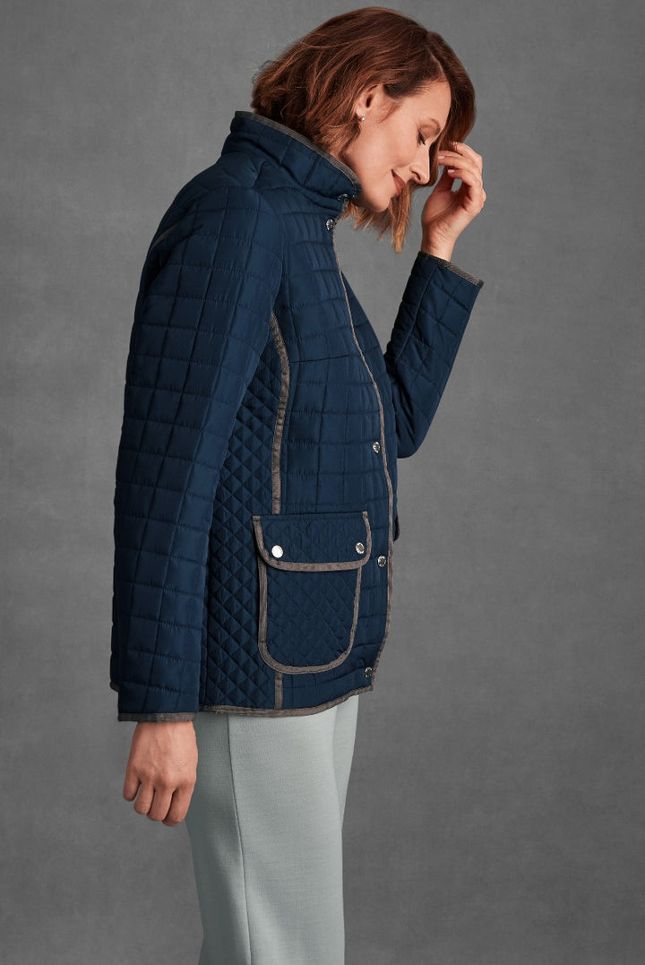 Lily Ella Collection stylish navy blue quilted jacket with high collar and detailed pocket design, paired with light grey trousers for a casual chic look.
