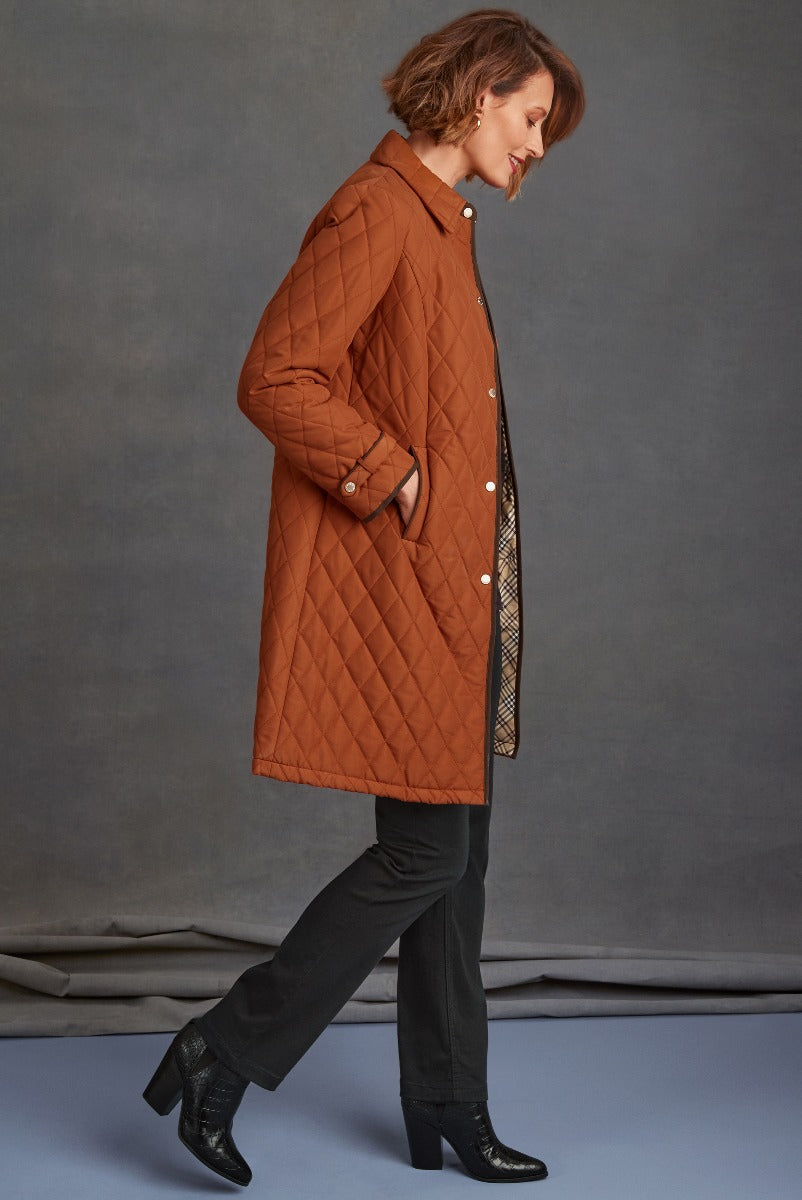 Lily Ella Collection model wearing a stylish rust-colored quilted coat with button details and side pockets, paired with black trousers and textured ankle boots for a sophisticated autumn look.