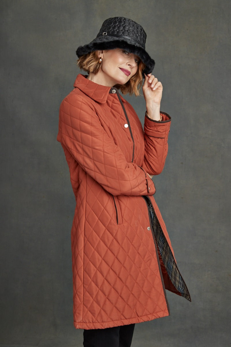 Lily Ella Collection trendy burnt orange quilted coat with stylish black hat, women's fall fashion outerwear, chic modern autumn look.