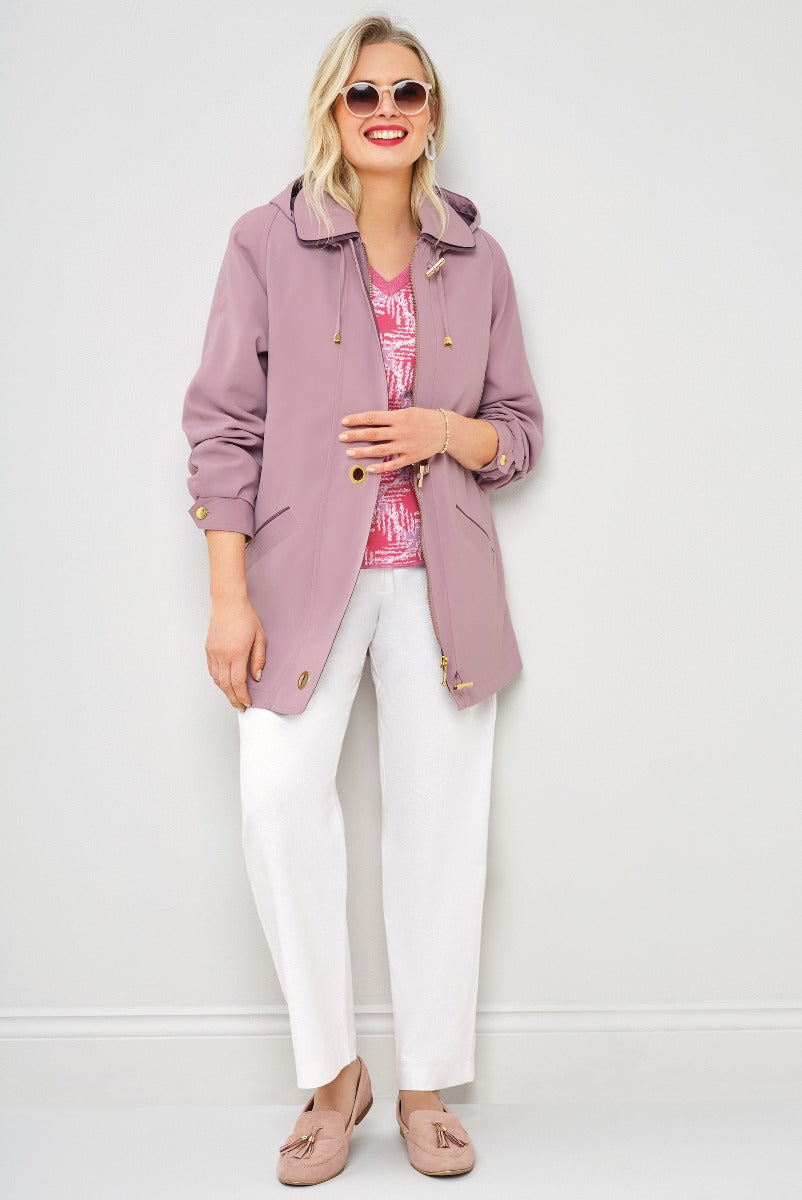 Lily Ella Collection - Stylish woman in mauve casual jacket with adjustable hood paired with white trousers and pink patterned blouse, accessorized with tassel loafers and oversized sunglasses.