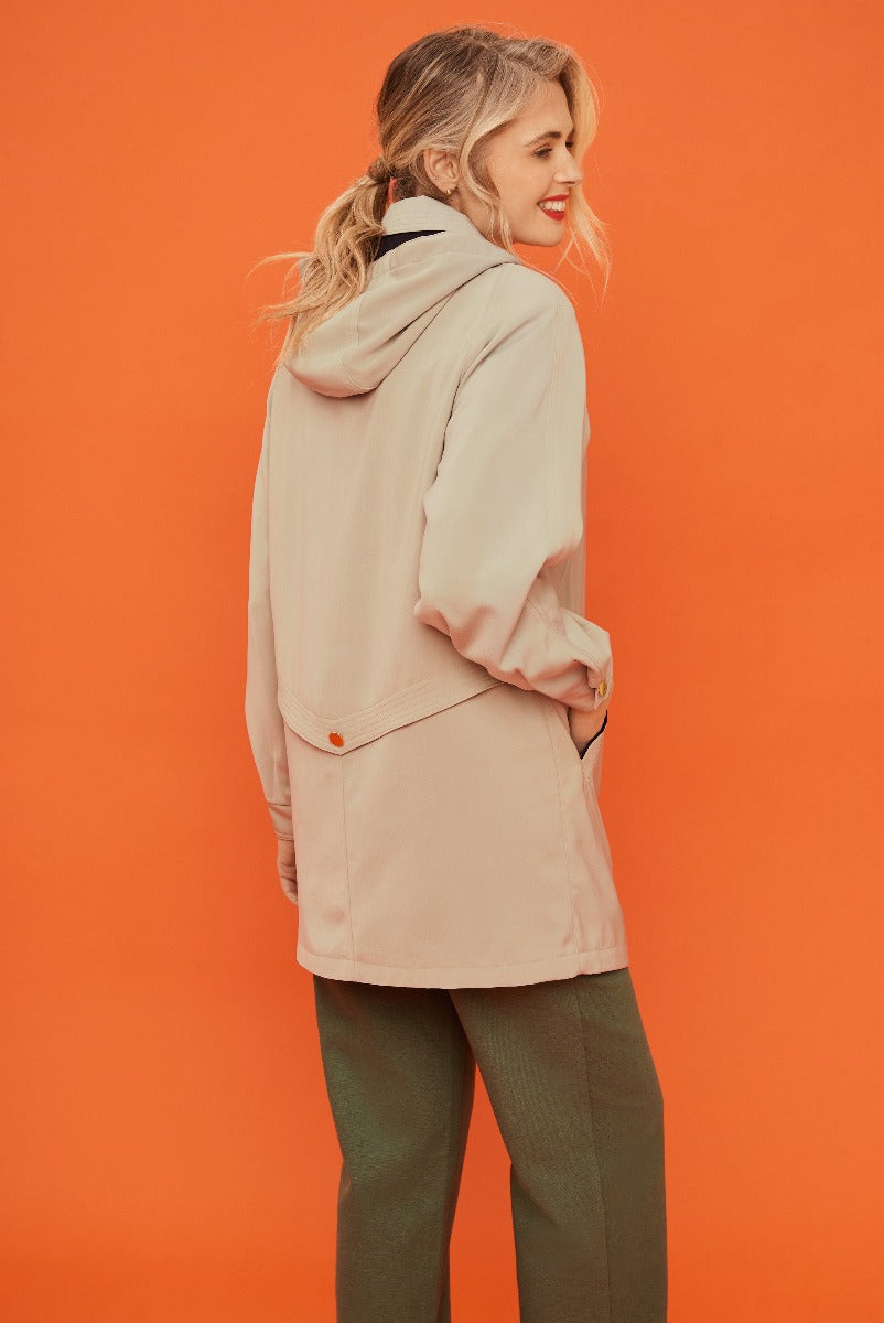 Lily Ella Collection beige casual jacket paired with olive trousers on smiling female model against orange background.