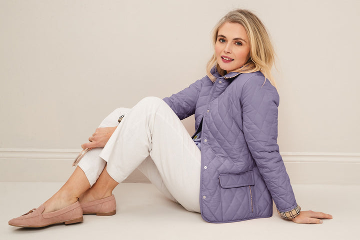 Lily Ella Collection lavender quilted jacket with a stylish collar, white trousers, and pink loafers, fashion model in a relaxed pose showcasing casual elegant women's wear.