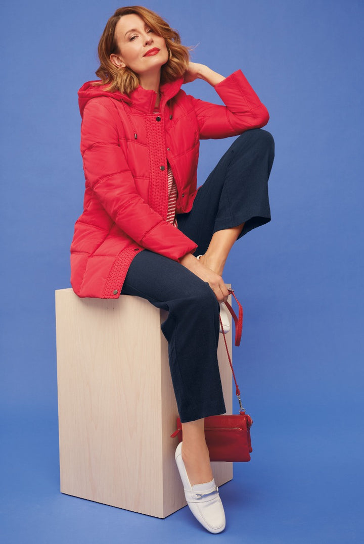 Lily Ella Collection red quilted jacket, fashion model wearing stylish winter outerwear, contrasting blue background, outfit complemented with navy trousers, white loafers, and red shoulder bag