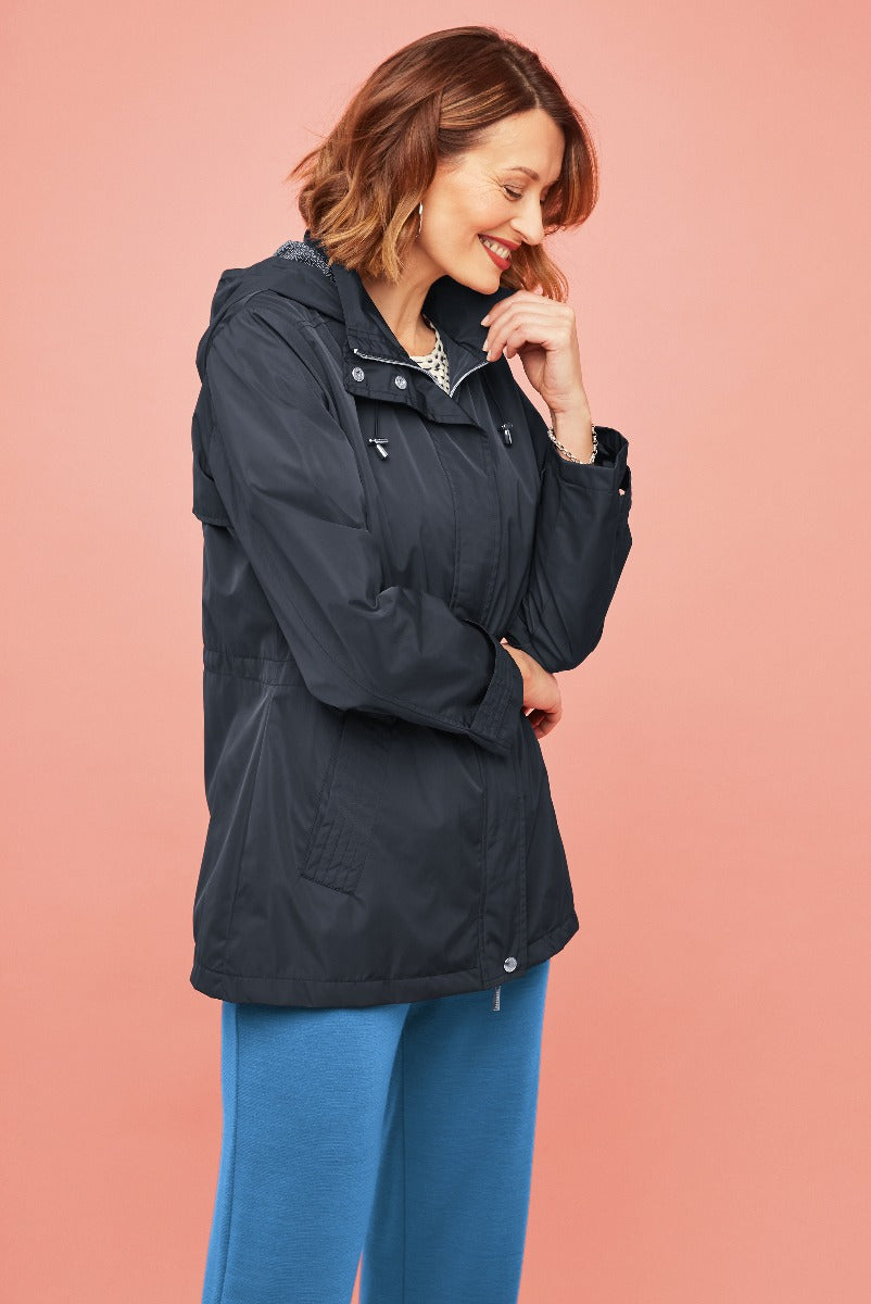 Lily Ella Collection stylish navy waterproof jacket with patterned collar on smiling model against pink background, paired with blue trousers, casual chic outerwear for women.