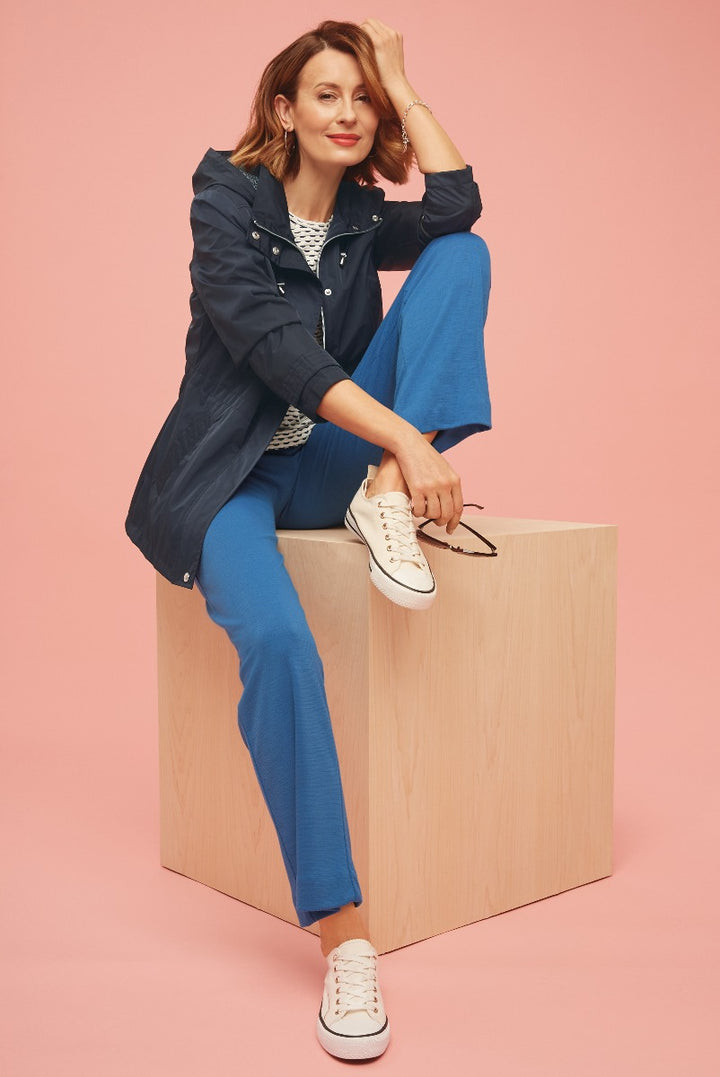Lily Ella Collection chic casual outfit featuring navy raincoat, graphic tee, and vibrant blue trousers paired with white sneakers against a pink background