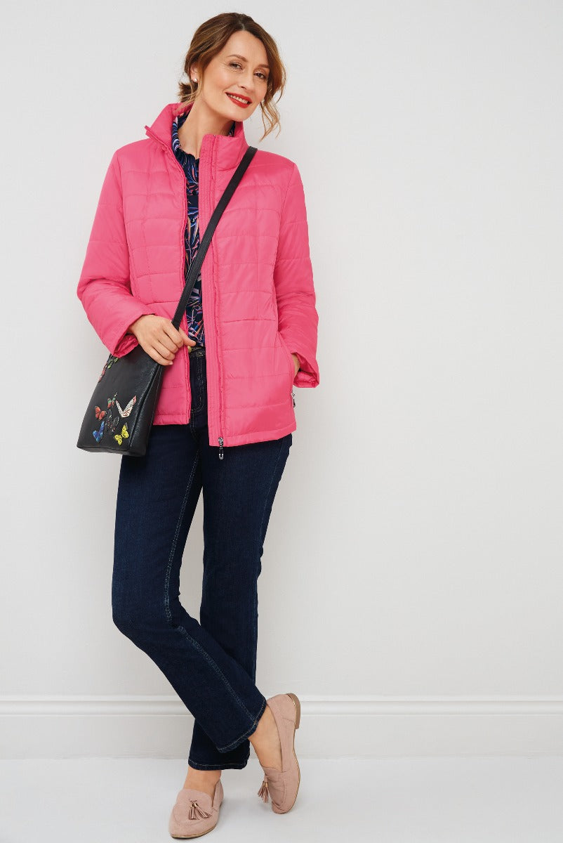 Lily Ella Collection vibrant pink quilted jacket, stylish navy denim jeans, and chic beige ballet flats, featuring a model with crossbody embellished purse