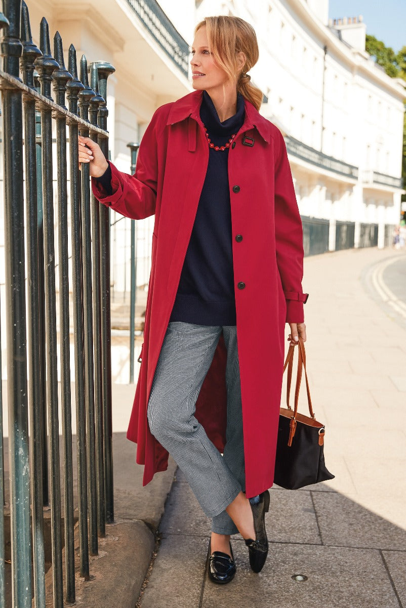 Lily Ella Collection vibrant red trench coat styled with navy sweater and patterned trousers, elegant urban fashion for women, accessorized with black loafers and leather tote bag.