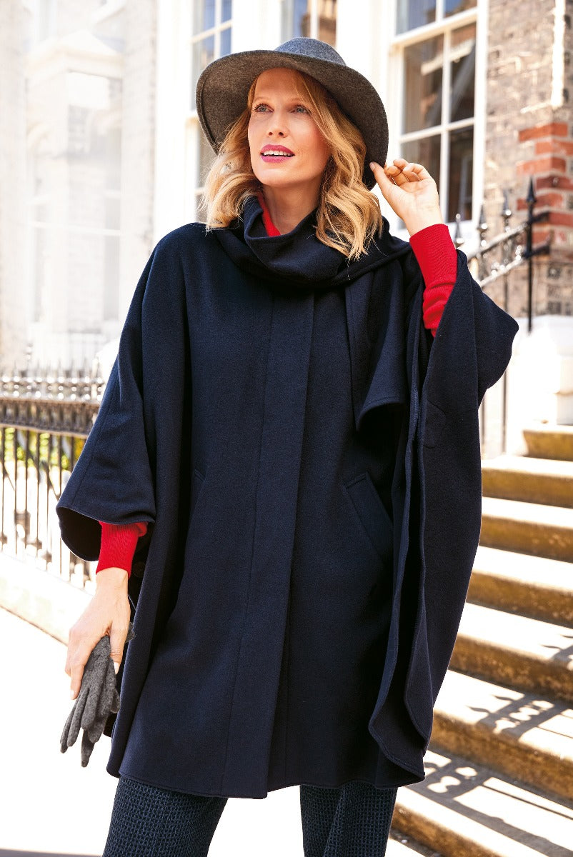 Lily Ella Collection elegant navy blue cape-style coat, woman wearing stylish autumn-winter outerwear with red sweater and chic wide-brimmed hat, classic and sophisticated fashion look.