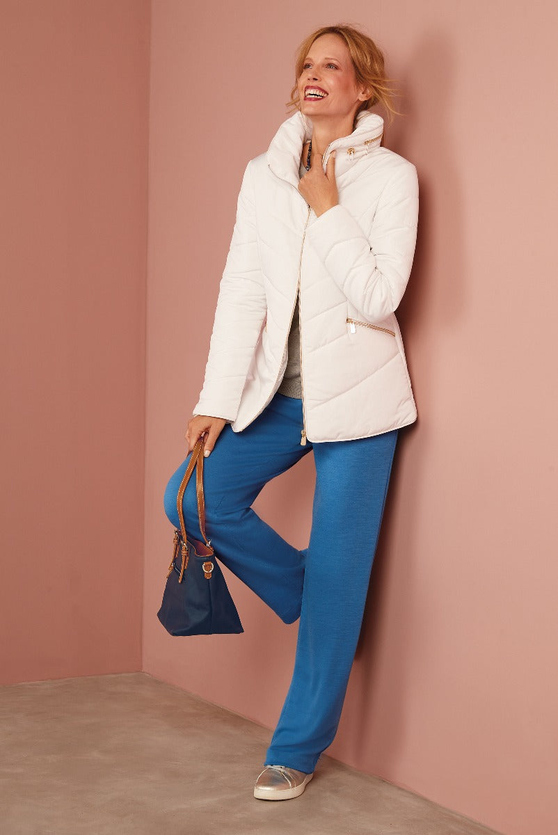 Lily Ella Collection elegant white quilted jacket and vibrant blue trousers, stylish casual women's attire with shoulder bag and sneakers.