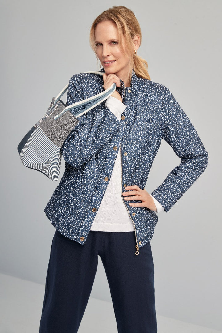 Lily Ella Collection fashion model wearing a stylish navy blue floral print jacket with button details, coordinated with a white sweater, navy trousers, and a chic striped handbag.