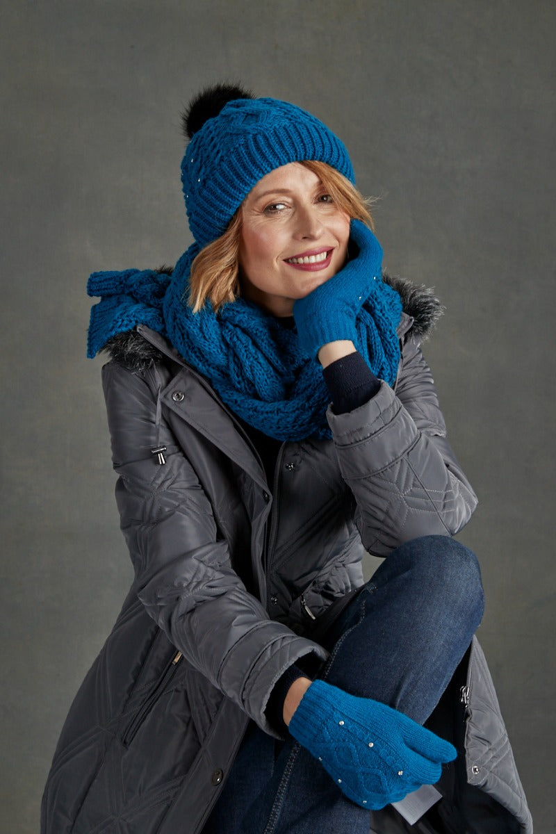 Lily Ella Collection - Woman in stylish grey quilted coat with vibrant blue knitted beanie and scarf accessorized with matching gloves, cozy winter fashion.