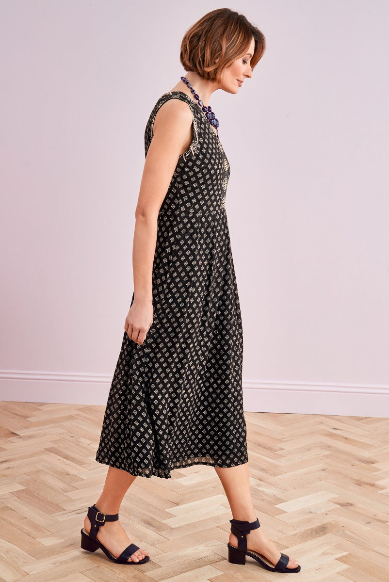 Lily Ella Collection black patterned sleeveless midi dress styled with purple bead necklace and black strapped heels on wooden floor
