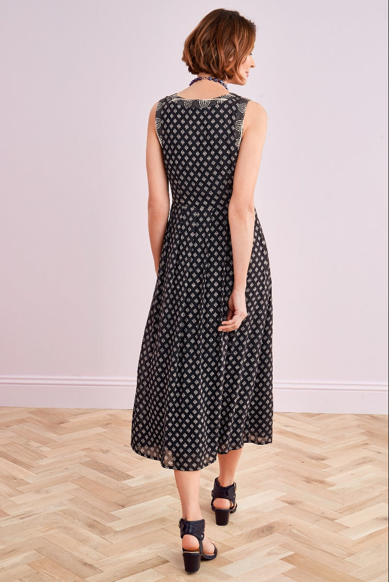 Lily Ella Collection women's fashion, rear view of a model wearing a patterned black mid-length dress paired with high-heeled sandals on a wooden floor with a pink wall background