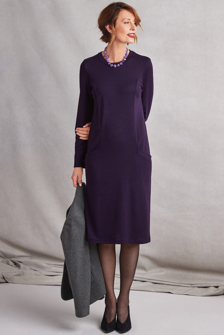 Lily Ella Collection elegant plum purple tunic dress with pockets, styled with black tights, heels and gray coat, featuring a statement necklace and subtle makeup for a sophisticated look.