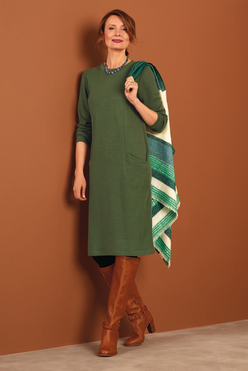 Lily Ella Collection olive green tunic dress for women featuring relaxed fit, side pockets, and three-quarter sleeves, paired with brown leather boots and a striped shoulder wrap, accessorized with a blue necklace.