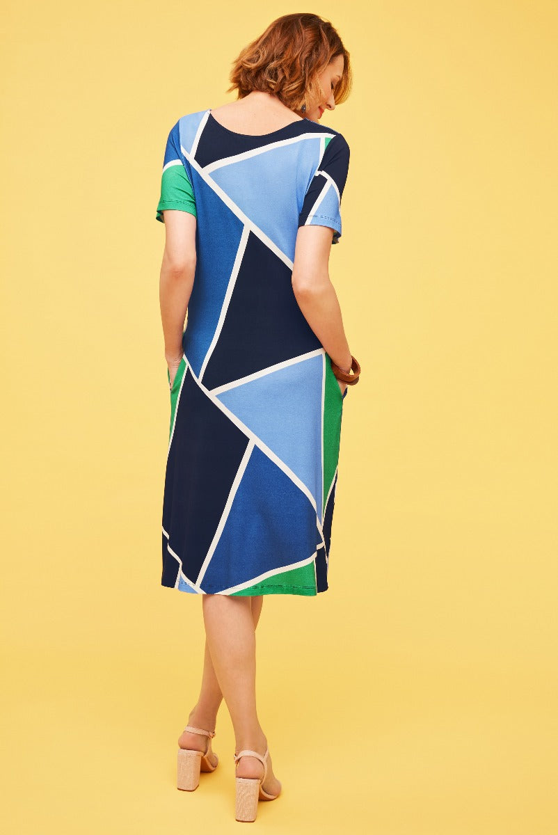 Lily Ella Collection geometric pattern dress in blue, green, and white, stylish knee-length design with short sleeves, model posing with back to the camera on a yellow background, perfect for spring and summer fashion.