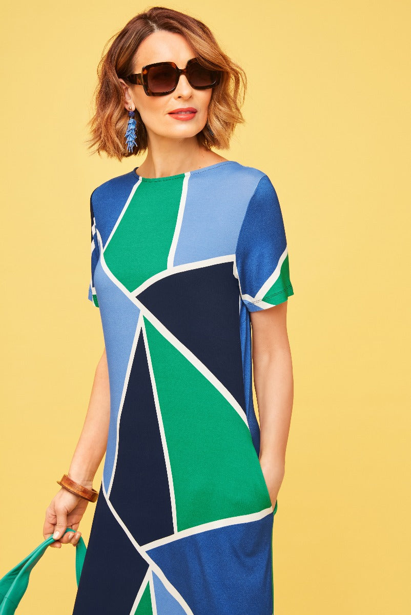 Lily Ella Collection geometric print dress in blue and green, stylish summer wear, model with sunglasses and statement earrings, vibrant yellow background.